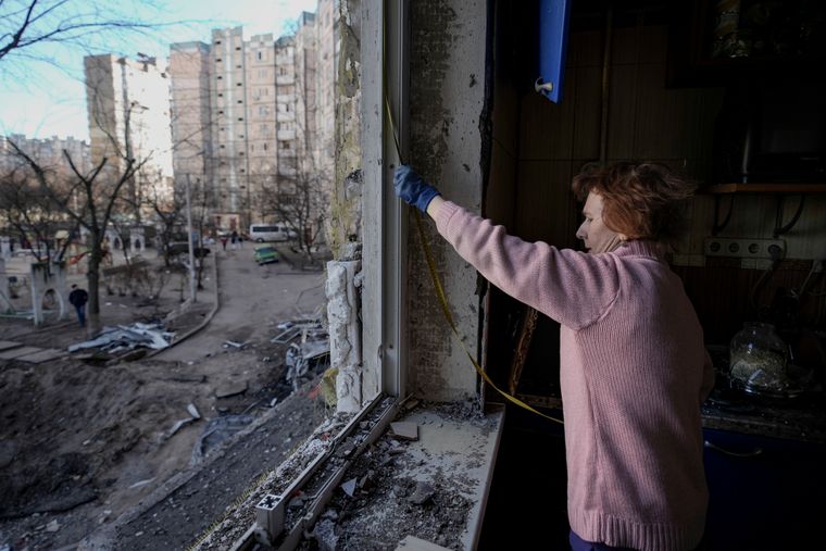 Жінка міряє вибите вікно у пошкодженій бомбардуванням будівлі, Київ, 21 березня 2022 року Фото: AP Photo/Vadim Ghirda