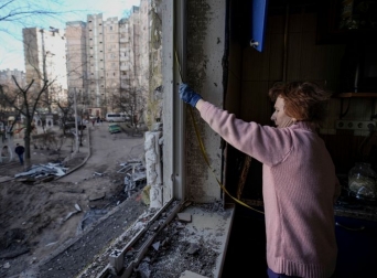 Жінка міряє вибите вікно у пошкодженій бомбардуванням будівлі, Київ, 21 березня 2022 року Фото: AP Photo/Vadim Ghirda